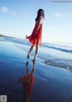 A woman in a red dress walking on the beach.