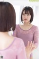 A woman in a pink leotard looking at herself in the mirror.