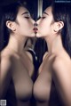 A couple of women kissing in front of a mirror.