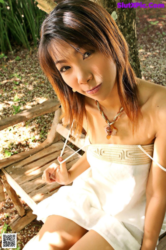 A woman in a white dress sitting on a wooden bench.