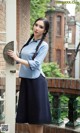 A woman in a blue shirt and black skirt leaning against a wall.