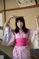 A woman in a pink kimono holding an orange in her hand.