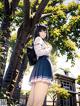 A girl in a school uniform standing in front of a tree.