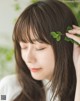 A woman with long brown hair holding a green leaf in her hair.